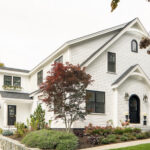 A white house featuring black trim, accompanied by a neatly paved driveway leading to the entrance.