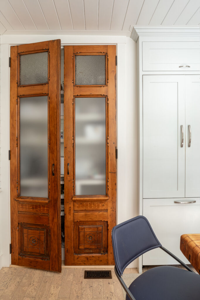 Vintage wood-paneled French doors with frosted glass inserts, opening to a pantry, beside floor-to-ceiling white built-in cabinets
